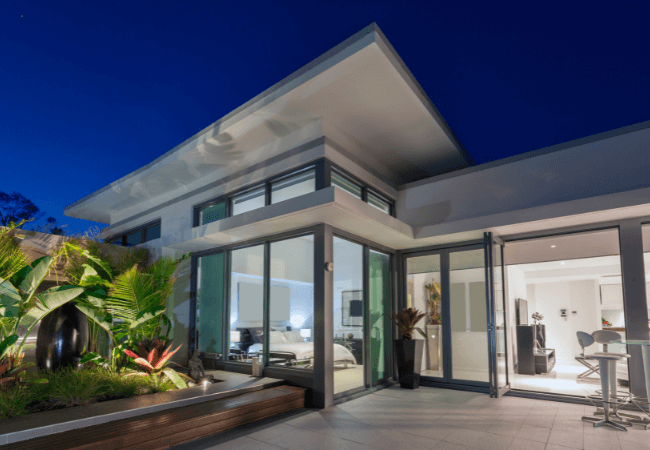 New-Kitchen Modern luxury home exterior at night with large glass windows, a well-lit interior, and lush landscaping.