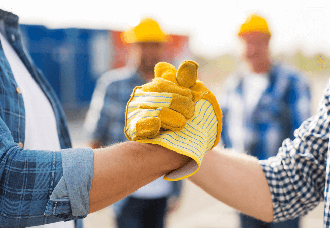 Construction workers in protective gear shaking hands on site, signifying teamwork