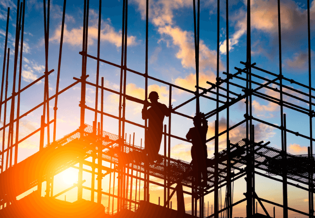 Silhouetted construction workers on scaffolding at sunset, representing project management in action